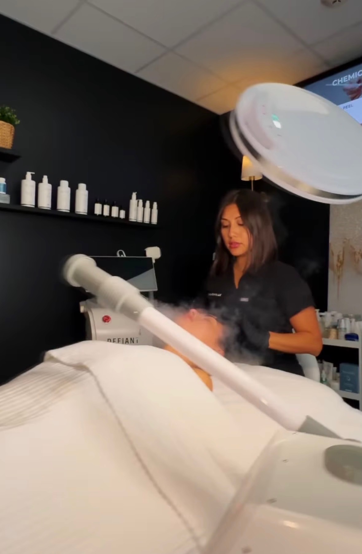 An esthetician performing a medical-grade facial in the treatment room at Defiant Health in Lisle, IL